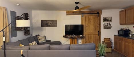 Una sala de estar con un sofá, un televisor, un aparador de madera y una mesa de comedor con una botella.
