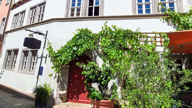 Un bâtiment avec une porte rouge, de nombreuses fenêtres et un balcon doté de balustrades.