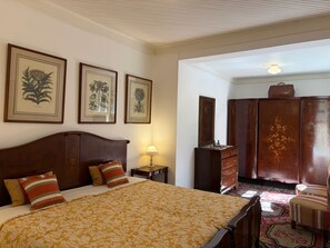 A bedroom with a bed, a dresser, a lamp, and framed botanical prints on the wall. - Historic Mansion With Fireplace in Campos do Jord o (Campos do Jordão)