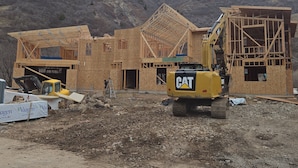 A construction site with a partially built wooden structure, a yellow CAT excavator, and a worker on a ladder. - Provo Riverhouse 6 King Beds Sleeps 24 Hot Tub Sauna (Provo)