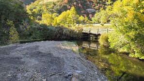 Une rivière traversée par un pont en bois, entourée d’une végétation luxuriante et bordée de rochers au premier plan.