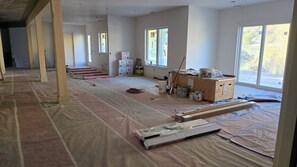 A spacious room with large windows, a wooden floor, and construction materials scattered around.