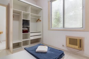 Una stanza con un armadio bianco, una finestra dotata di zanzariera e un termosifone a parete.