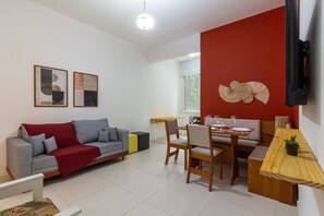 Ein modernes Wohnzimmer mit einem grauen Sofa, einem Esstisch mit Stühlen und einer roten Akzentwand.