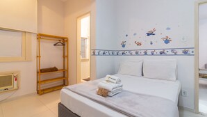 Ett hotellrum med en säng, en hylla i trä, en väggmonterad värmare och ett fönster.