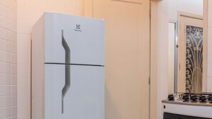 Ett kök med ett vitt kylskåp, en spis och ett vitt kaklat golv.