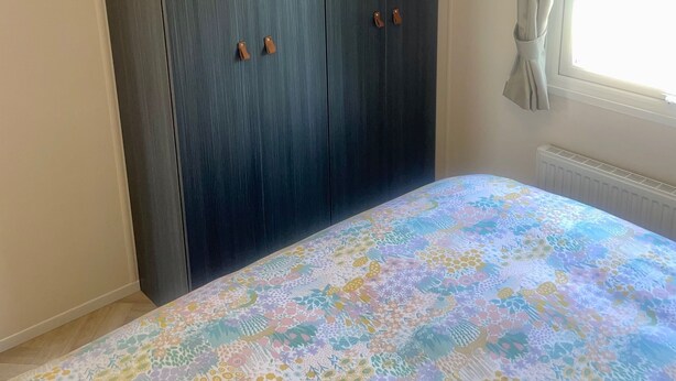 A bedroom with a bed, a wardrobe, and a window with curtains.