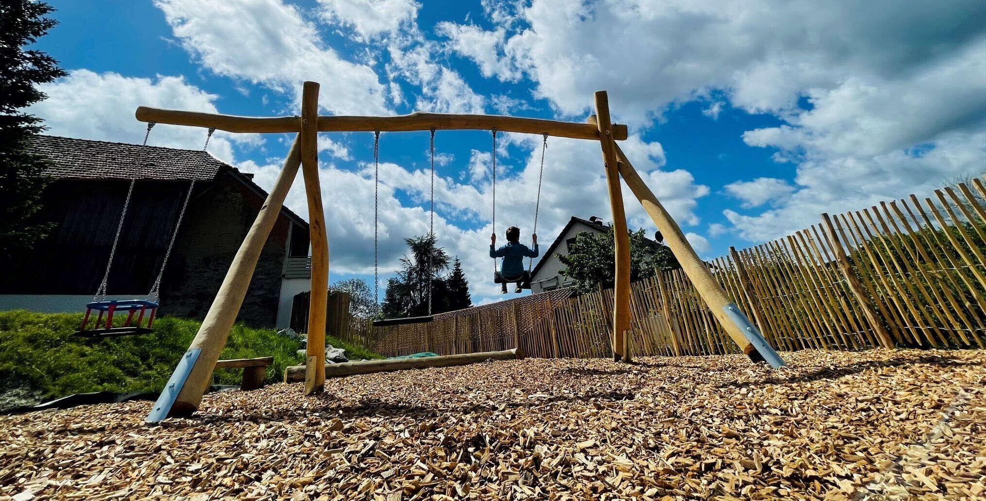 A wooden swing set in a backyard with a house and a fence in the background.