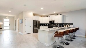 Una cocina moderna con armarios blancos, una isla central y taburetes de bar.