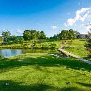 Um campo de golfe com lago, árvores e um edifício ao fundo.