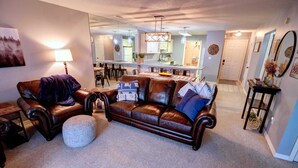 A living room with a brown leather sofa, a round ottoman, and a dining area with a table and chairs. - Welcome to Relaxation Pointe at Pointe Royale in Branson, Missouri! (Branson)