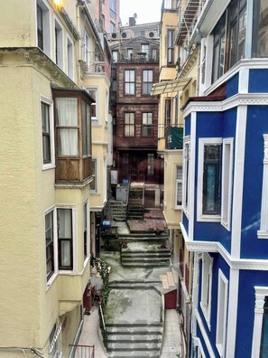 A narrow alleyway between buildings with a staircase leading to a second-floor entrance. - Redecorated Flat With Huge Library 100mbps (Istanbul)