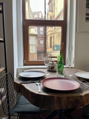 A dining table set with plates, cutlery, and glasses, positioned by a window with a view of buildings. - Redecorated Flat With Huge Library 100mbps (Istanbul)