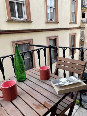 A wooden table with two red mugs and a green bottle, a wooden chair, and a magazine on the table. - Redecorated Flat With Huge Library 100mbps (Istanbul)