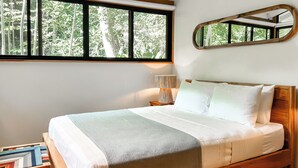 Quarto com uma janela grande, luminária de cabeceira, espelho e mesa de cabeceira com livros.