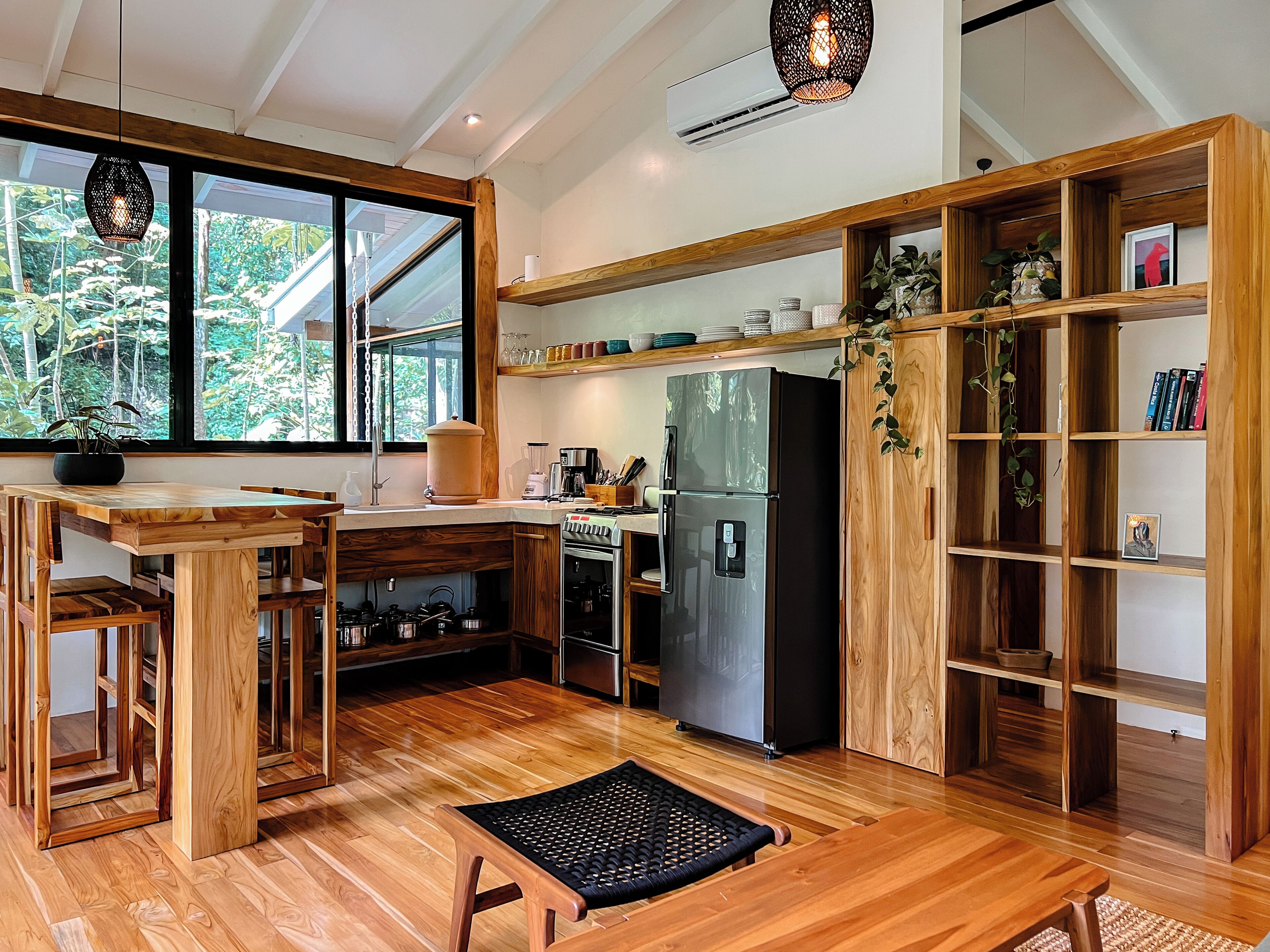 A modern kitchen with wooden cabinetry, a large island, and a view of greenery outside.