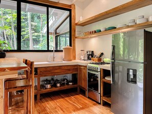 Une cuisine avec des meubles en bois, une cuisinière, un réfrigérateur et une fenêtre donnant sur les arbres.