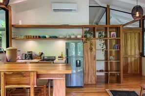 A modern kitchen with wooden shelves, a stainless steel refrigerator, and a dining area with a wooden table and chairs.