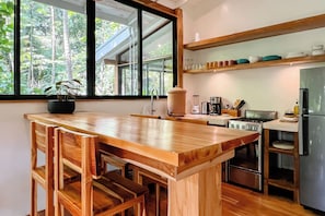 A kitchen with a wooden island, stainless steel appliances, and a view of the forest through large windows.