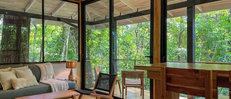 A spacious room with a large sliding glass door leading to an outdoor deck, a wooden bench, a sofa, and a table.