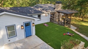 A house with a blue door, a stone chimney, a covered patio, and a well-maintained lawn. - Lake Hartwell Home + Cottage, Private Dock, Hot Tub, Game Room with pool table! (Hartwell)