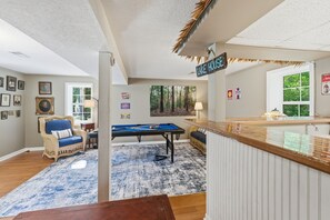 A room with a pool table, a lounge chair, a bar area, and a view of a forest. - Lake Hartwell Home + Cottage, Private Dock, Hot Tub, Game Room with pool table! (Hartwell)