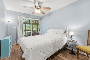 A bedroom with a bed, a nightstand, a lamp, a chair, a ceiling fan, and a window with curtains. - Lake Hartwell Home + Cottage, Private Dock, Hot Tub, Game Room with pool table! (Hartwell)