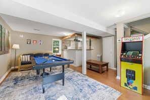 A room with a pool table, a sofa, a coffee table, and a Pac-Man arcade machine. - Lake Hartwell Home + Cottage, Private Dock, Hot Tub, Game Room with pool table! (Hartwell)