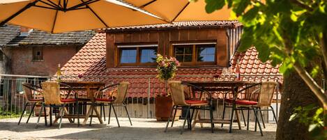 A patio with outdoor seating, a large umbrella, and a building with a tiled roof.
