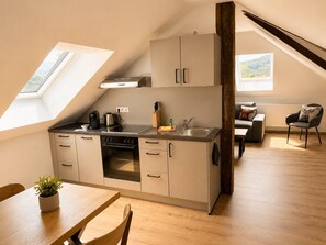 Una cocina moderna con tragaluz, un comedor con mesa y sillas de madera, y una sala de estar con sofá y sillón.