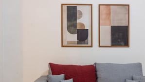 Una sala moderna con un sofá gris, una manta roja y dos cuadros abstractos en la pared.