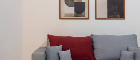 A modern living room with a grey sofa, red throw blanket, and two abstract paintings on the wall.