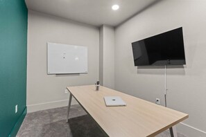 Ein Konferenzraum mit einer Whiteboard, einem Flachbildfernseher, einem Laptop auf einem Tisch und einem Teppichboden.