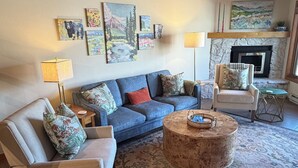 Ein Wohnzimmer mit einem blauen Sofa, einem runden Couchtisch, einem Kamin und einer Steinwand.