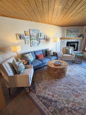 Ein Wohnzimmer mit einem blauen Sofa, einem runden Couchtisch, einem Kamin und einer Steinwand.