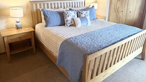 Ein Schlafzimmer mit einem hölzernen Bett, einem Nachttisch, einer Lampe, einem Bild an der Wand und einem Kleiderschrank.