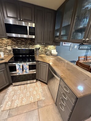 A modern kitchen with dark cabinetry, stainless steel appliances, a patterned rug, and a blue wall with a framed picture. - Elevated Oasis-3BR-Mt. CB-Garage-Hot Tub-Mountain Views (Crested Butte)