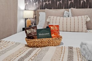 Habitación de hotel con cama, libreta de bienvenida y una cesta con aperitivos.