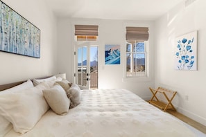 A bedroom with a large bed, two windows with views, and artwork on the walls. - Rooftop Views, Walk to Downtown, Sleeps 13 (Buena Vista)