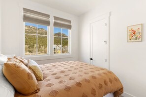 A bedroom with a bed, two windows with blinds, a door, and a framed floral artwork on the wall. - Rooftop Views, Walk to Downtown, Sleeps 13 (Buena Vista)