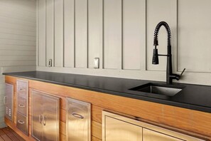 A kitchen with a black countertop, stainless steel cabinets, a black faucet, and a white wall with a light switch. - Rooftop Views, Walk to Downtown, Sleeps 13 (Buena Vista)