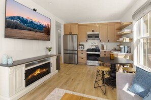 A modern kitchen with a fireplace, stainless steel appliances, wooden cabinets, and a large TV mounted on the wall. - Mountain Views | Apt Walk to Downtown | Sleeps 6 (Buena Vista)