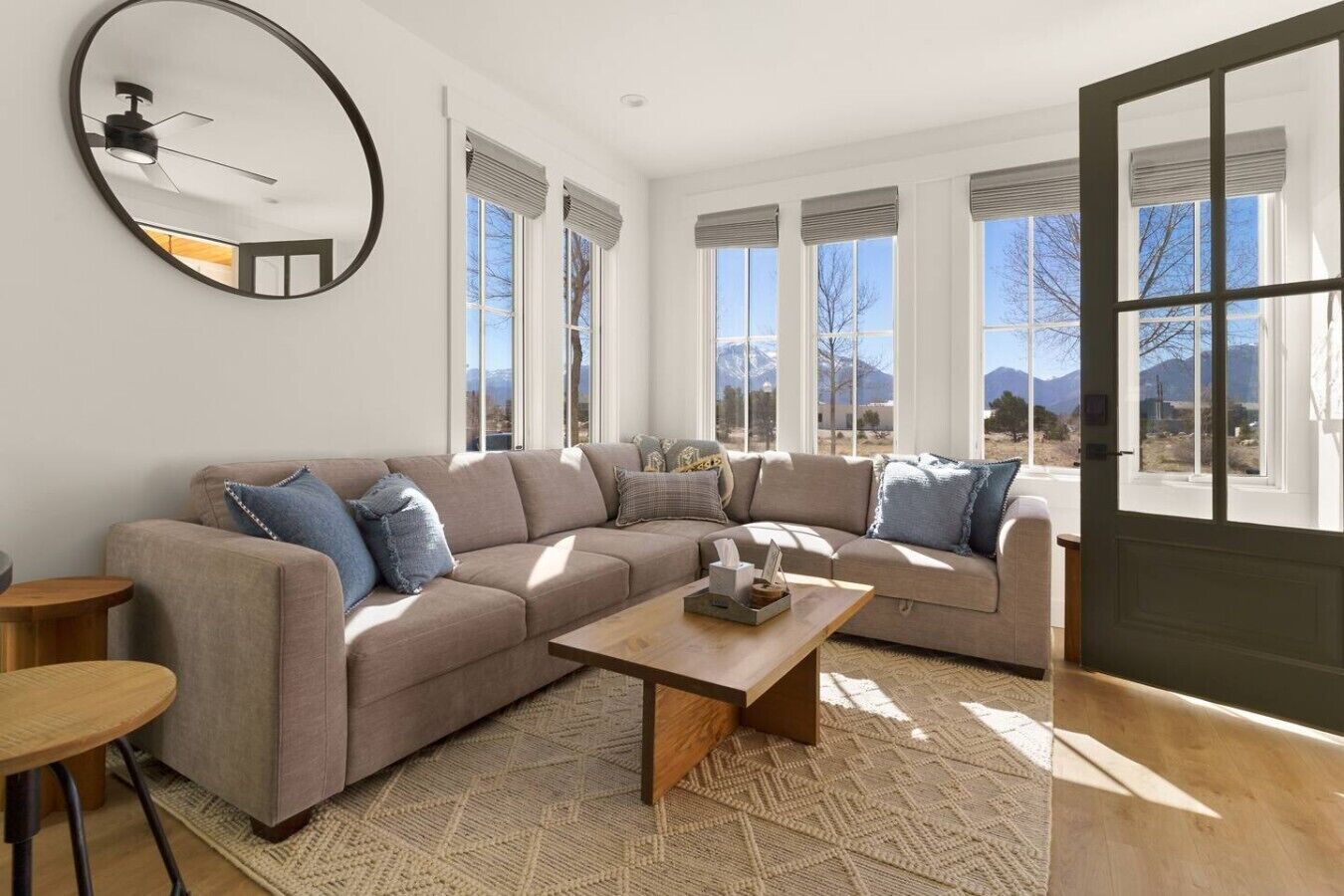 A living room with a sectional sofa, a round mirror, and a wooden coffee table.