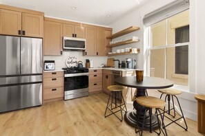 A modern kitchen with stainless steel appliances, wooden cabinets, and a round dining table with stools. - Mountain Views | Apt Walk to Downtown | Sleeps 6 (Buena Vista)