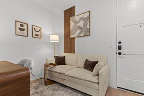Une chambre d’hôtel avec un canapé, une lampe, un mur recouvert de panneaux en bois et deux œuvres d’art encadrées.