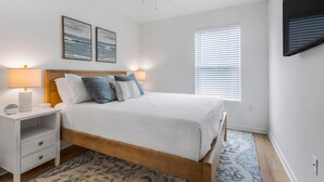 A bedroom with a bed, nightstands, a ceiling fan, wall art, a window with blinds, and a patterned rug. - Lost Bay Townhome 4239 (Orange Beach)