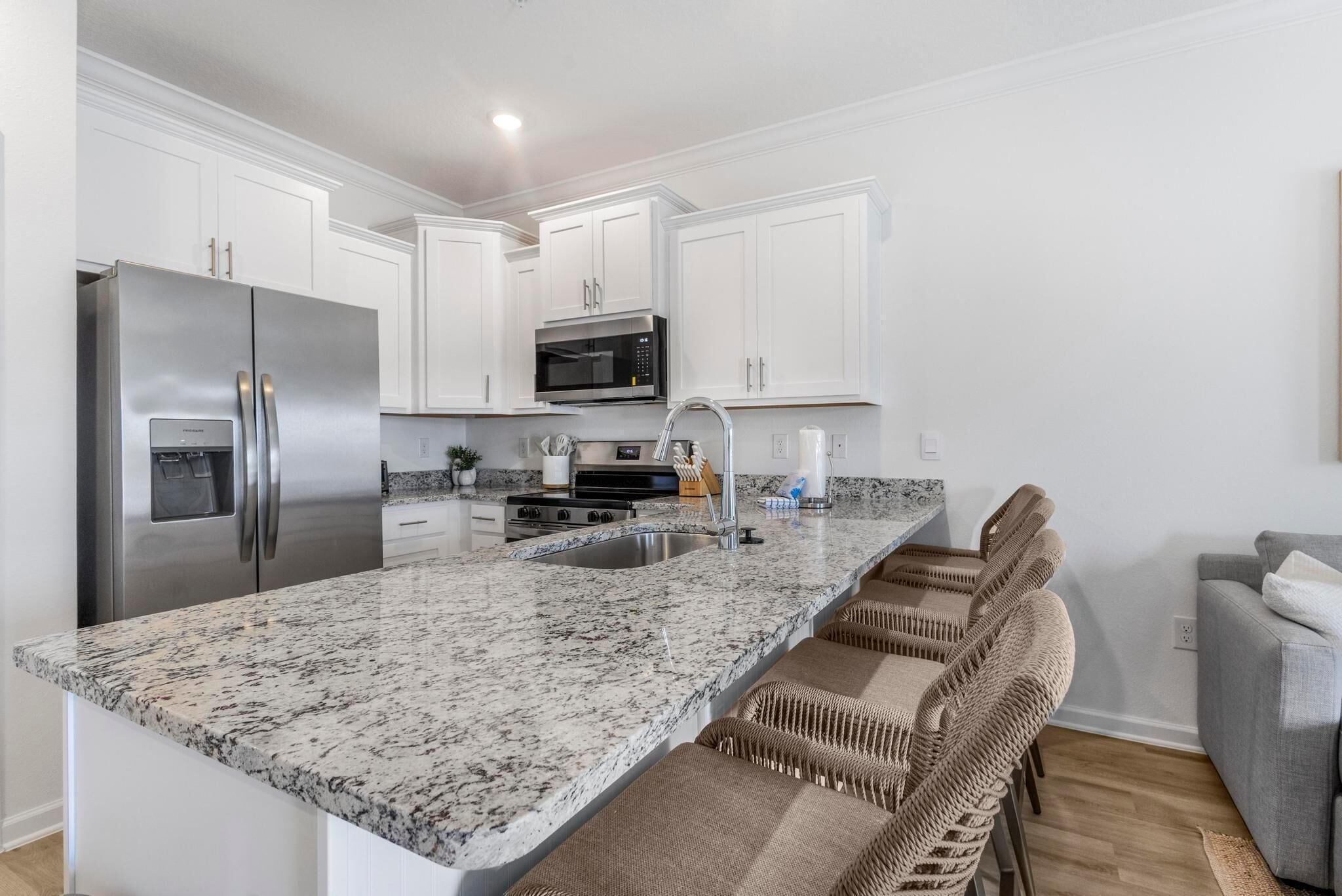 A modern kitchen with white cabinetry, stainless steel appliances, a granite countertop, and a built-in island with bar stools.