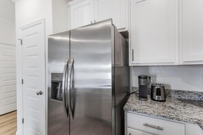 Ein Edelstahl-Kühlschrank, eine Kaffeemaschine und ein Toaster stehen auf einer Granit-Arbeitsplatte in einer Küche mit weißen Schränken.