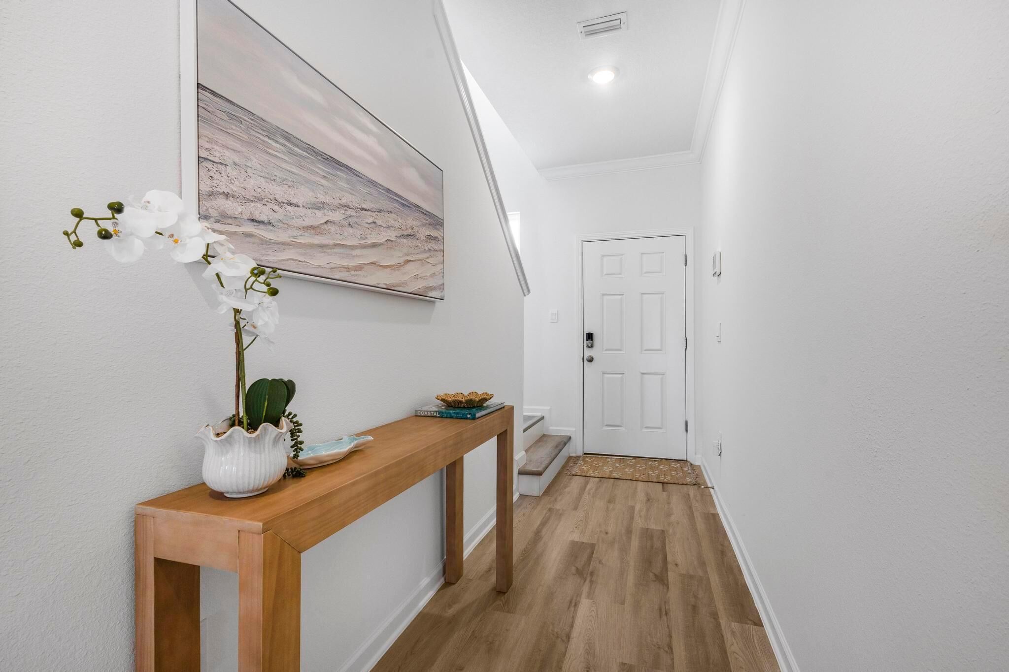 A hallway with a wooden console table, a potted plant, and a painting on the wall.