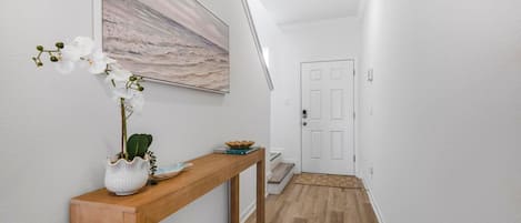 A hallway with a wooden console table, a potted plant, and a painting on the wall.